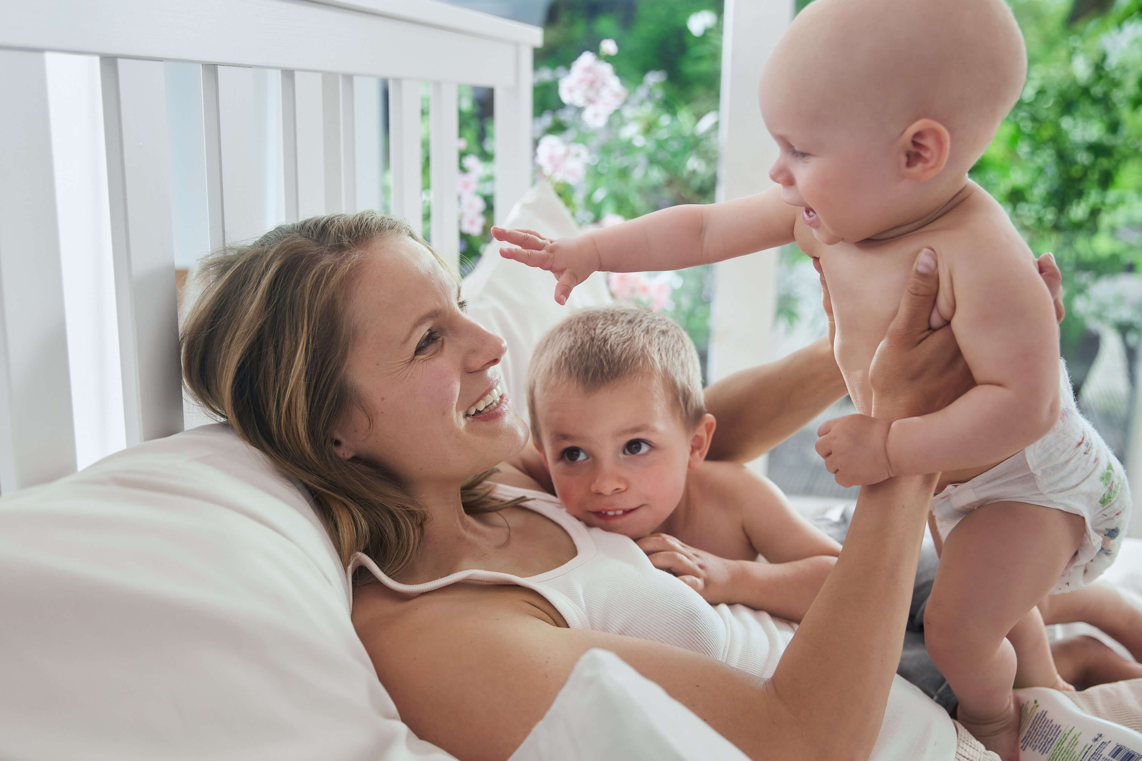 Ein freudiger Moment zwischen einer Frau und zwei Babys, wobei die Frau ein Baby im Arm hält, während das andere Baby die Hand nach ihr ausstreckt.