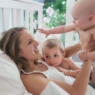 Ein freudiger Moment zwischen einer Frau und zwei Babys, wobei die Frau ein Baby im Arm hält, während das andere Baby die Hand nach ihr ausstreckt.