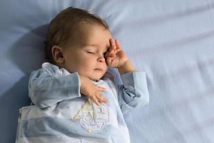 Ein Baby, das scheinbar tief schläft und dessen Gesicht von einer Hand sanft berührt wird.