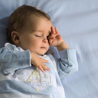 Ein Baby, das scheinbar tief schläft und dessen Gesicht von einer Hand sanft berührt wird.