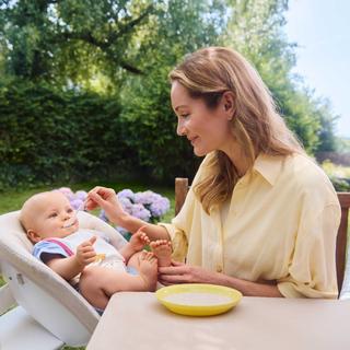 Mutter füttert ihr Baby im Garten mit Getreidebrei.