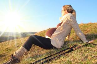 Eine Frau, die auf einem grasbewachsenen Hügel sitzt und in die Ferne blickt, vor einem sonnigen Hintergrund.