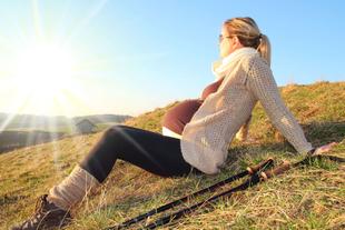 Eine Frau, die auf einem grasbewachsenen Hügel sitzt und in die Ferne blickt, vor einem sonnigen Hintergrund.