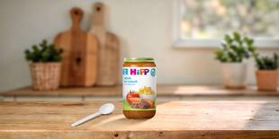 HiPP Bio Babygläschen Spätzle mit Gulasch 250g auf Holztisch, daneben ein Löffel in heller Küchenumgebung