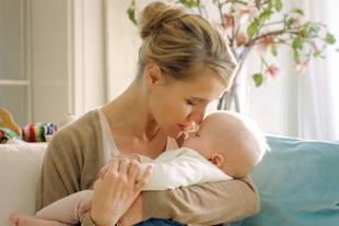 Ein zärtlicher Moment zwischen einer Mutter und ihrem Baby, in dem die Mutter sanft die Stirn des Babys küsst.