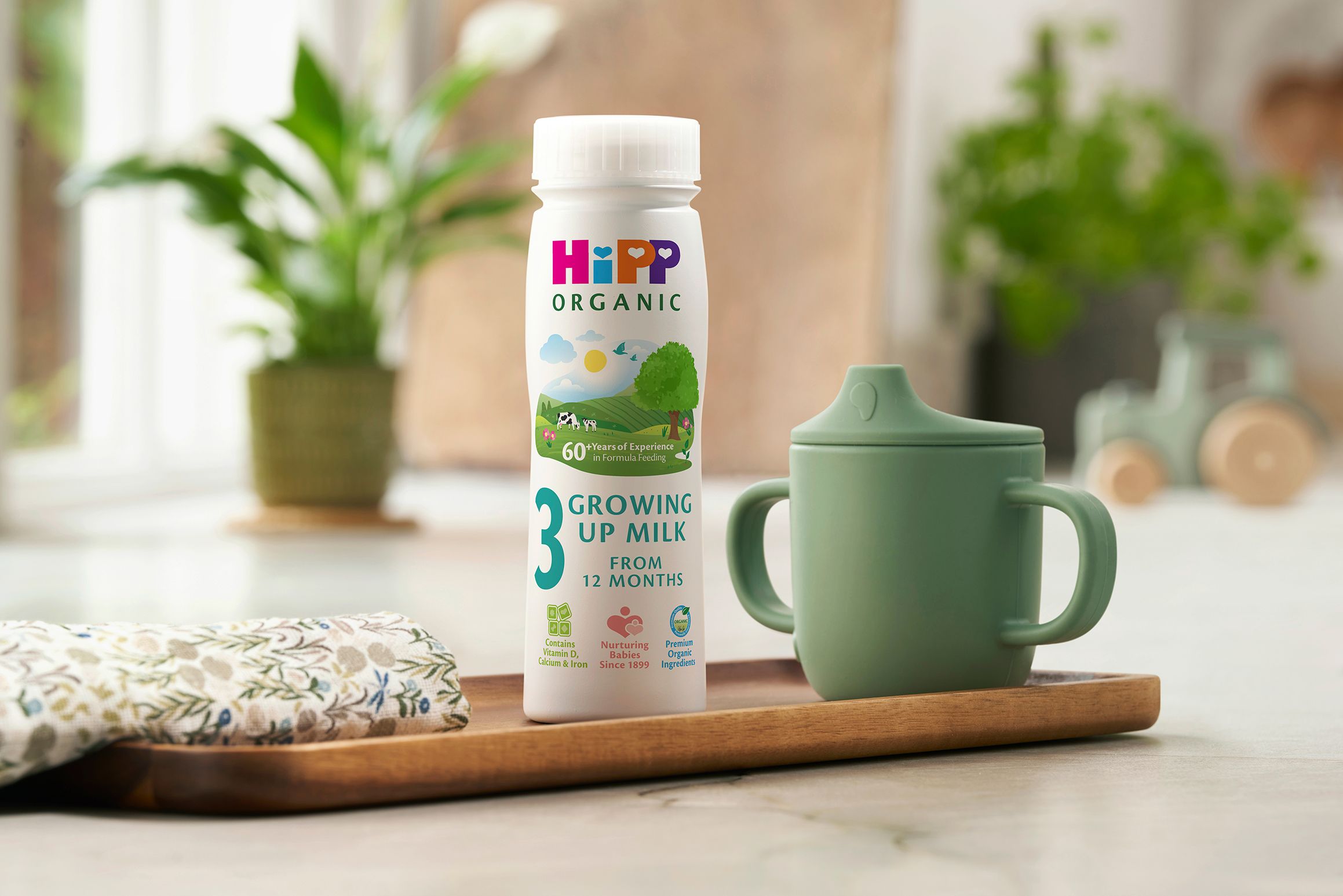 HiPP Organic Growing Up Milk ready-to-feed bottle on a kitchen tray beside a green toddler beaker