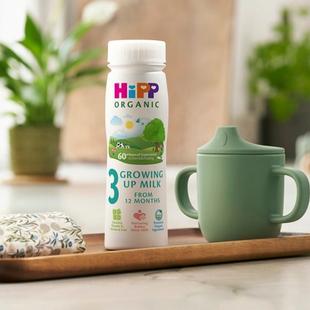 HiPP Organic Growing Up Milk ready-to-feed bottle on a kitchen tray beside a green toddler beaker