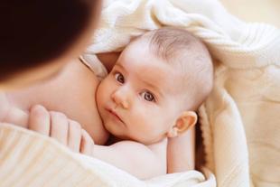 Ein zärtlicher Moment zwischen einer Mutter und ihrem Baby, wobei das Baby direkt in die Kamera schaut und die Hand der Mutter das Baby sanft wiegt.