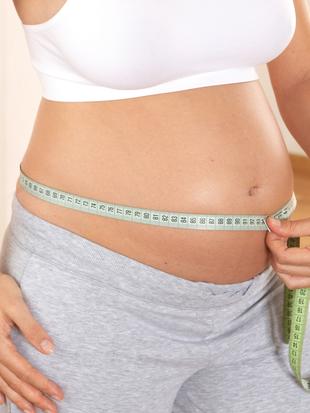 Eine Person misst ihren Bauch mit einem Maßband, wobei der Bauchbereich betont wird.