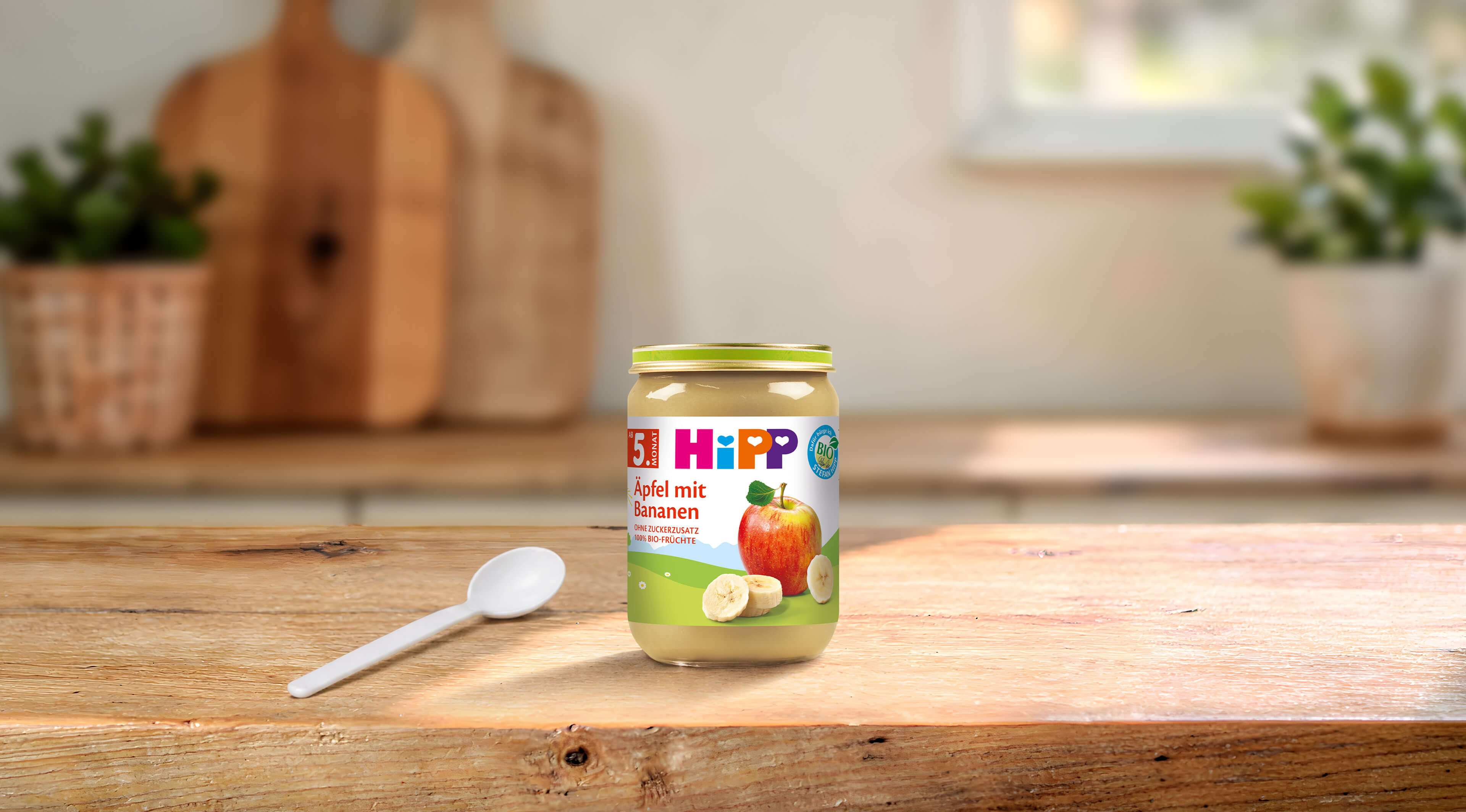 HiPP Bio Babygläschen Äpfel mit Bananen 190g auf Holztisch, daneben ein Löffel in heller, gemütlicher Küchenumgebung