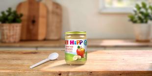 HiPP Bio Babygläschen Äpfel mit Bananen 190g auf Holztisch, daneben ein Löffel in heller, gemütlicher Küchenumgebung