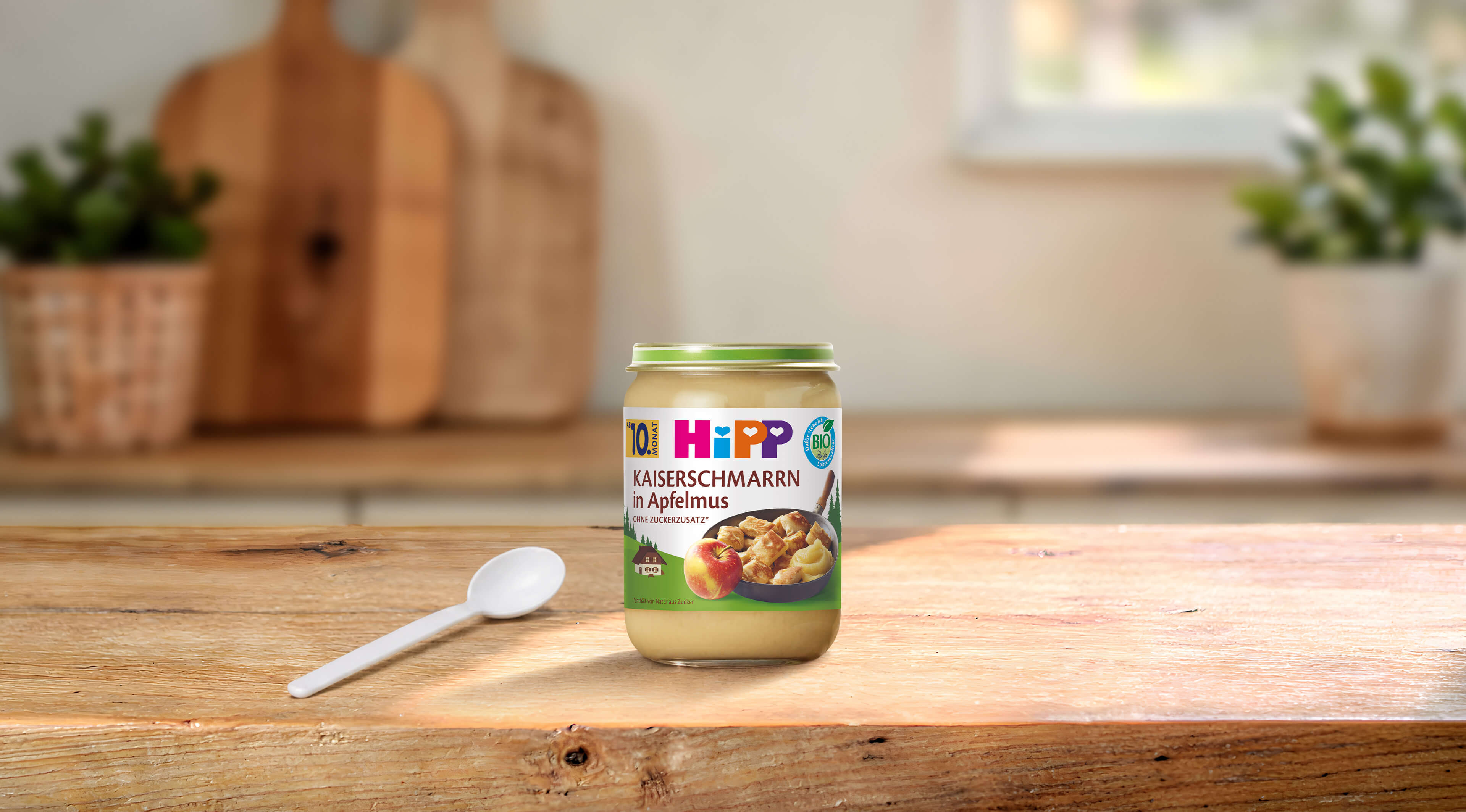 HiPP Bio-Gläschen Kaiserschmarrn in Apfelmus ab 10. Monat auf Holztisch mit Löffel in heller Küche