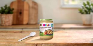 HiPP Bio-Gläschen Kaiserschmarrn in Apfelmus ab 10. Monat auf Holztisch mit Löffel in heller Küche