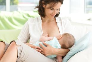 Eine Frau sitzt bequem auf einer Couch und stillt ihr Baby.