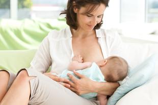 Eine Frau sitzt bequem auf einer Couch und stillt ihr Baby.