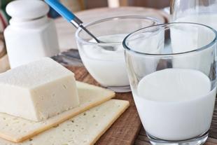 Verschiedene Molkereiprodukte, darunter ein Stück Käse, ein Glas Milch und ein Behälter mit Joghurt, die alle auf einer Holzunterlage platziert sind.