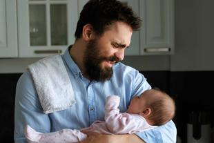 Ein zärtlicher Moment zwischen einem bärtigen Mann und einem Baby, in dem der Mann das Baby im Arm hält und beide eine freudige Interaktion teilen.