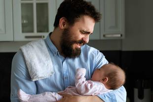 Ein zärtlicher Moment zwischen einem bärtigen Mann und einem Baby, in dem der Mann das Baby im Arm hält und beide eine freudige Interaktion teilen.