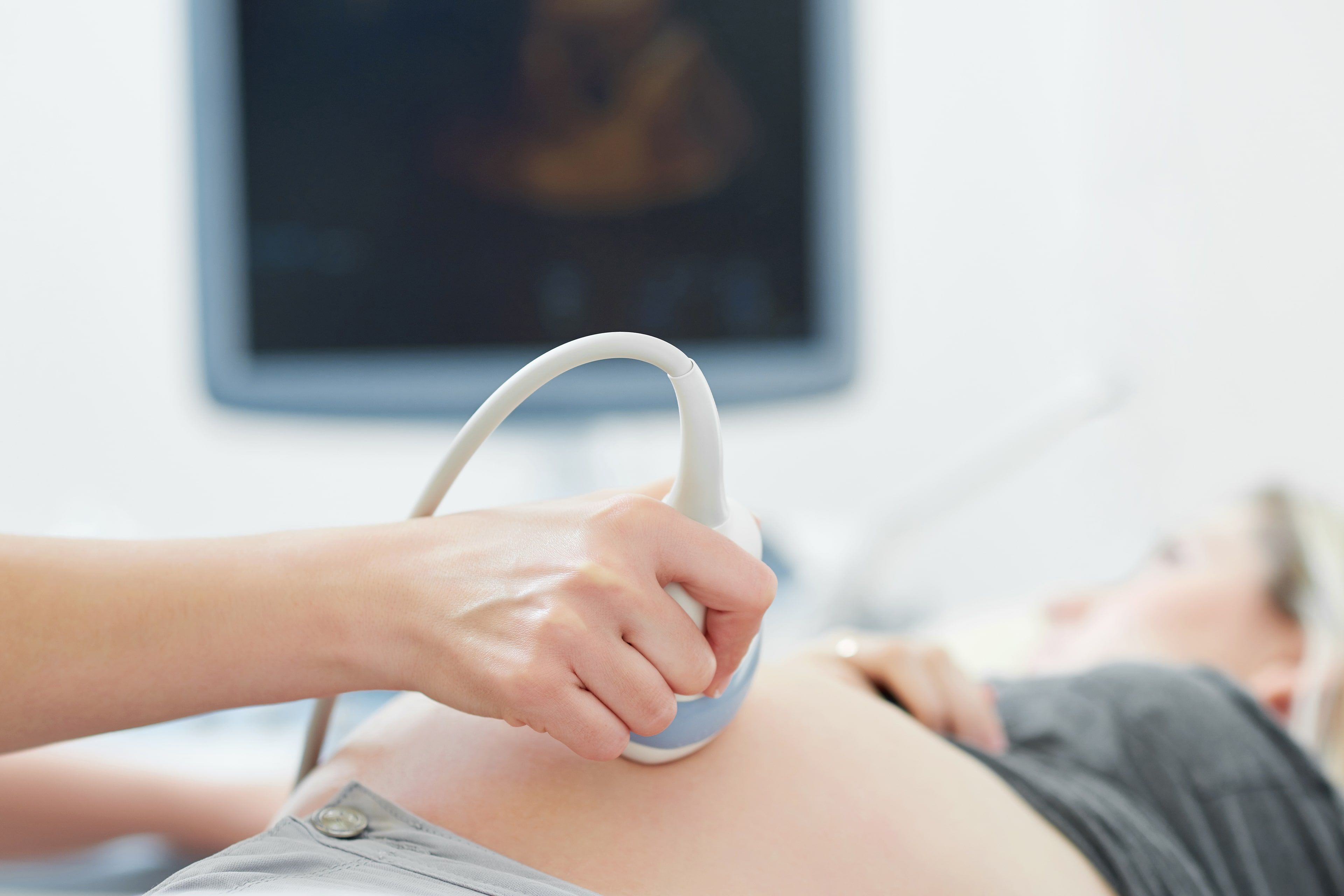 Eine medizinische Fachkraft, die während einer Ultraschalluntersuchung eine Sonde auf dem Bauch eines Patienten einsetzt.