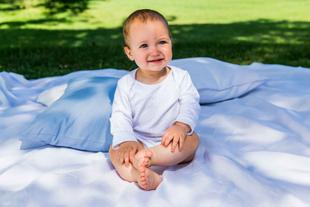 Ein fröhliches Baby, das auf einer weißen Decke in einer Umgebung mit Grünpflanzen und blauen Kissen sitzt.
