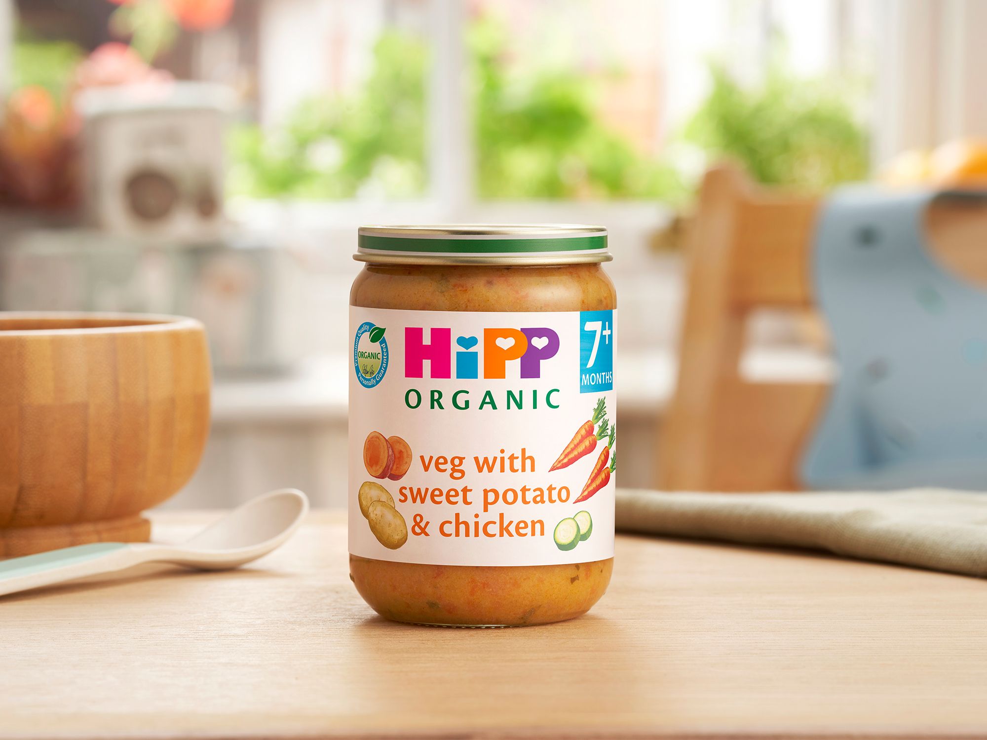 HiPP Organic Veg With Sweet Potato & Chicken Jar on a dining table next to a bowl and spoon
