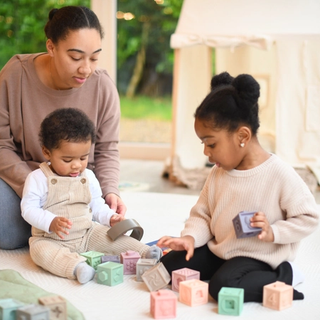 Toddler sharing toys with younger brother whilst mum watches over them