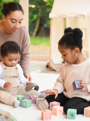Toddler sharing toys with younger brother whilst mum watches over them