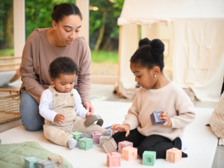 Toddler sharing toys with younger brother whilst mum watches over them