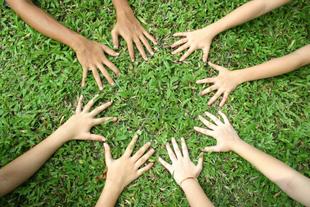 Mehrere Kinderhände bilden auf grüner Wiese einen Kreis als Symbol für Gemeinschaft und Verantwortung für die Natur