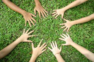 Mehrere Kinderhände bilden auf grüner Wiese einen Kreis als Symbol für Gemeinschaft und Verantwortung für die Natur