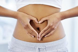 Eine Person formt eine Herzform mit ihren Händen über dem Bauch.