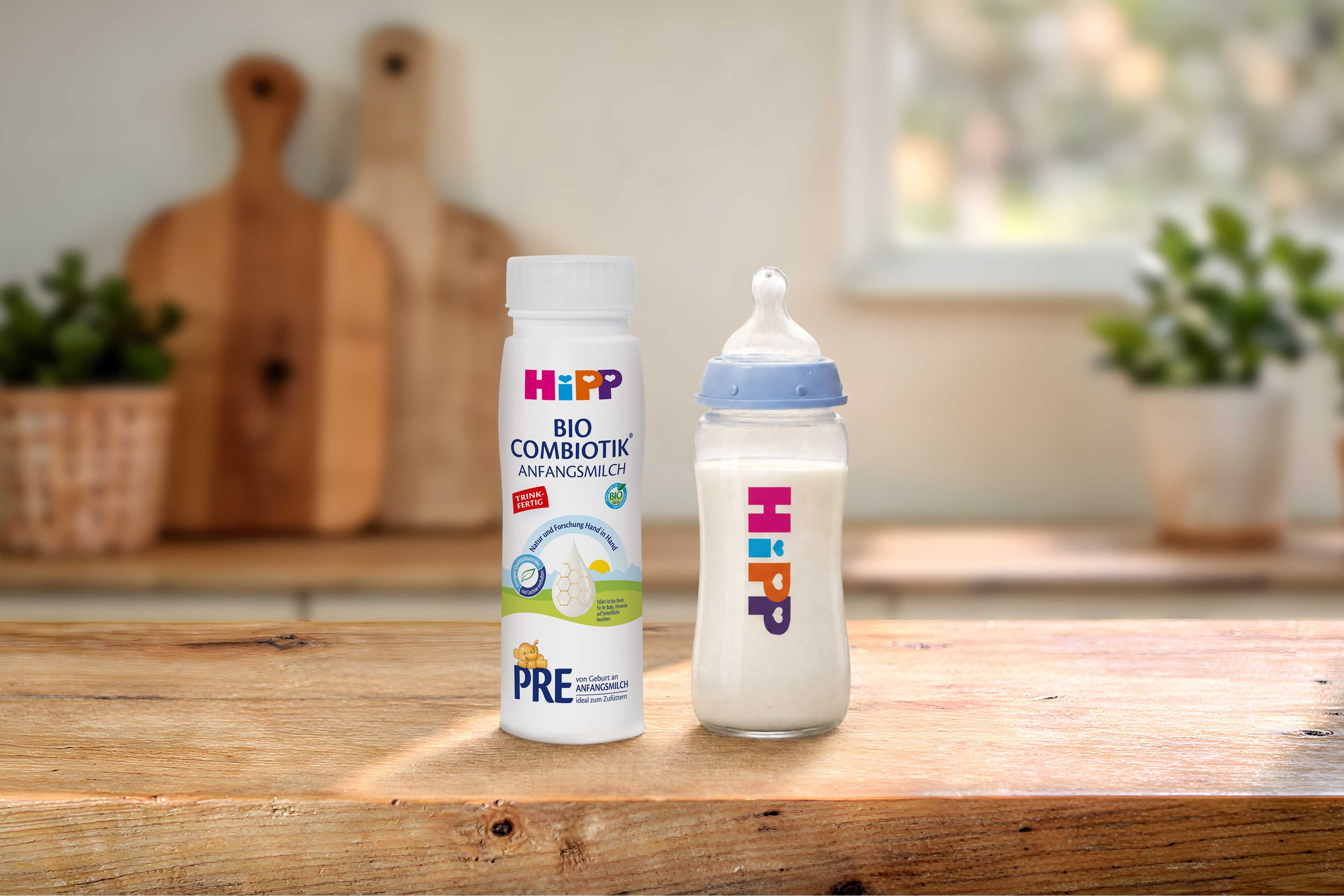 HiPP PRE BIO Combiotik® trinkfertige Anfangsmilchflasche neben gefülltem Babyfläschchen auf Holztisch in heller Küche