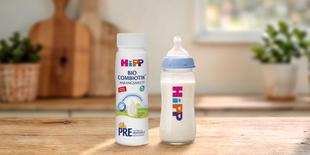HiPP PRE BIO Combiotik® trinkfertige Anfangsmilchflasche neben gefülltem Babyfläschchen auf Holztisch in heller Küche