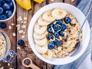 Eine Schüssel Haferflocken mit geschnittenen Bananen, Blaubeeren und Chiasamen, dazu ein Glas Haferflocken und eine Banane.