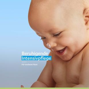 Lachendes Baby mit Creme auf der Nase vor blauem Hintergrund, Text: „Beruhigende Intensivpflege für trockene Haut“