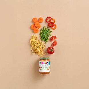 HiPP Organic Veg & Chicken Noodles jar with noodles, carrots, peas, peppers and tomatoes arranged above on a neutral background