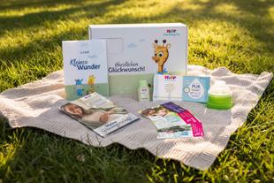 Produktpaket von HiPP Baby Club mit U-Heft Hülle, Broschüren, Produktproben, Milchportionierer und Geschenkbox auf einer Decke im Gras