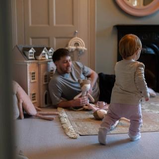 father laying on the floor holding a doll and playing with toddler.
