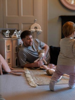 father laying on the floor holding a doll and playing with toddler.