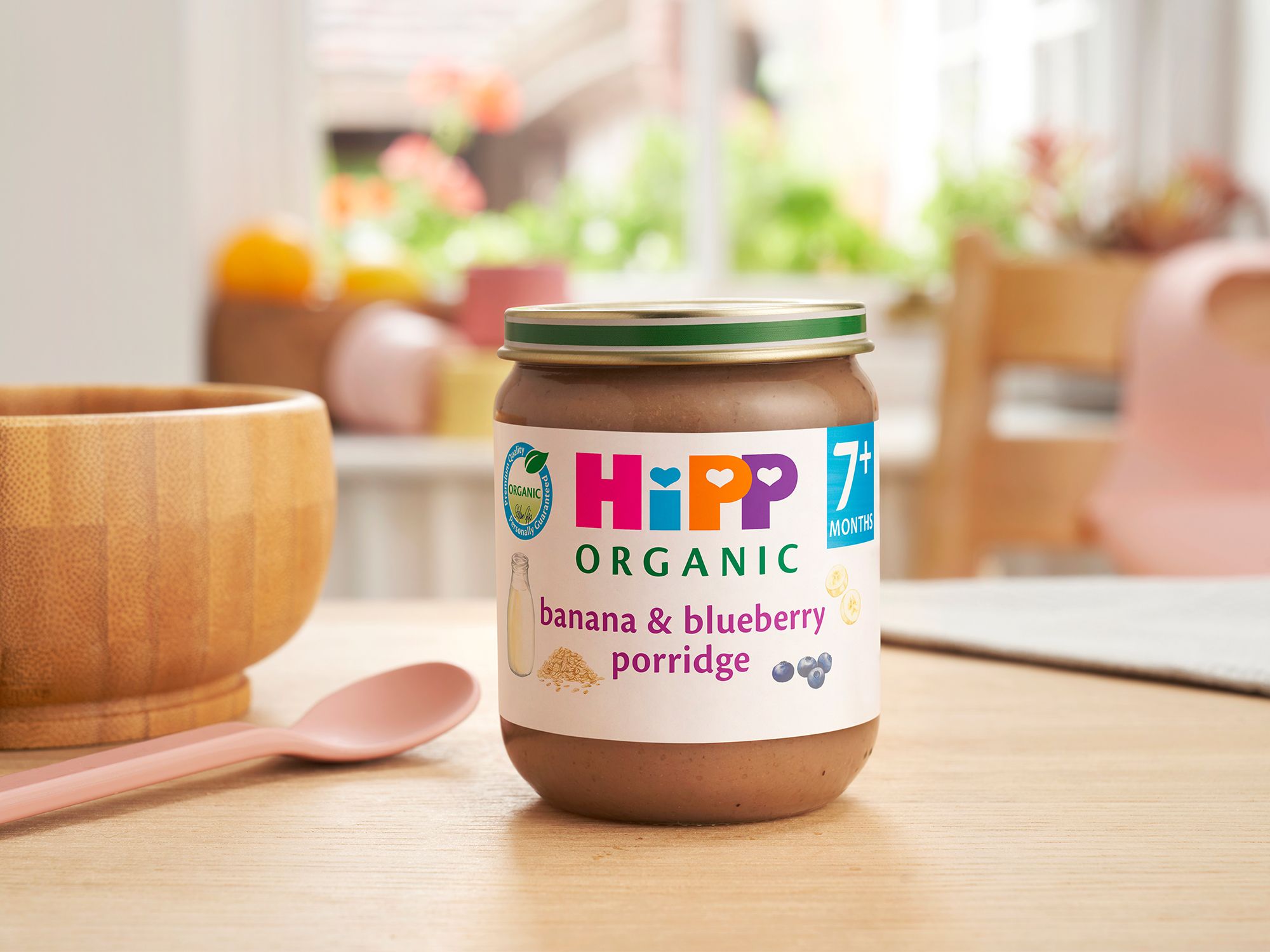 HiPP Organic Banana & Blueberry Porridge Jar on a dining table next to a bowl and spoon
