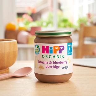 HiPP Organic Banana & Blueberry Porridge Jar on a dining table next to a bowl and spoon