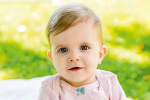 Ein Baby mit blauen Augen, das ein rosa Outfit trägt, vor einem leuchtend grünen Hintergrund.