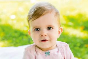 Ein Baby mit blauen Augen, das ein rosa Outfit trägt, vor einem leuchtend grünen Hintergrund.