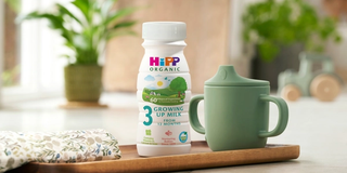 HiPP Organic growing up milk ready to feed bottle next to a beaker
