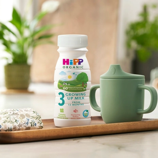 HiPP Organic growing up milk ready to feed bottle next to a beaker