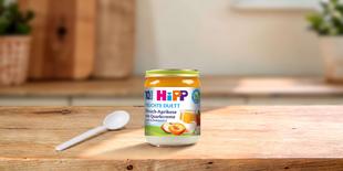 HiPP Früchte-Duett Bio-Gläschen Pfirsich-Aprikose mit Quarkcreme ab 10 Monaten auf Holztisch mit Löffel in heller Küche