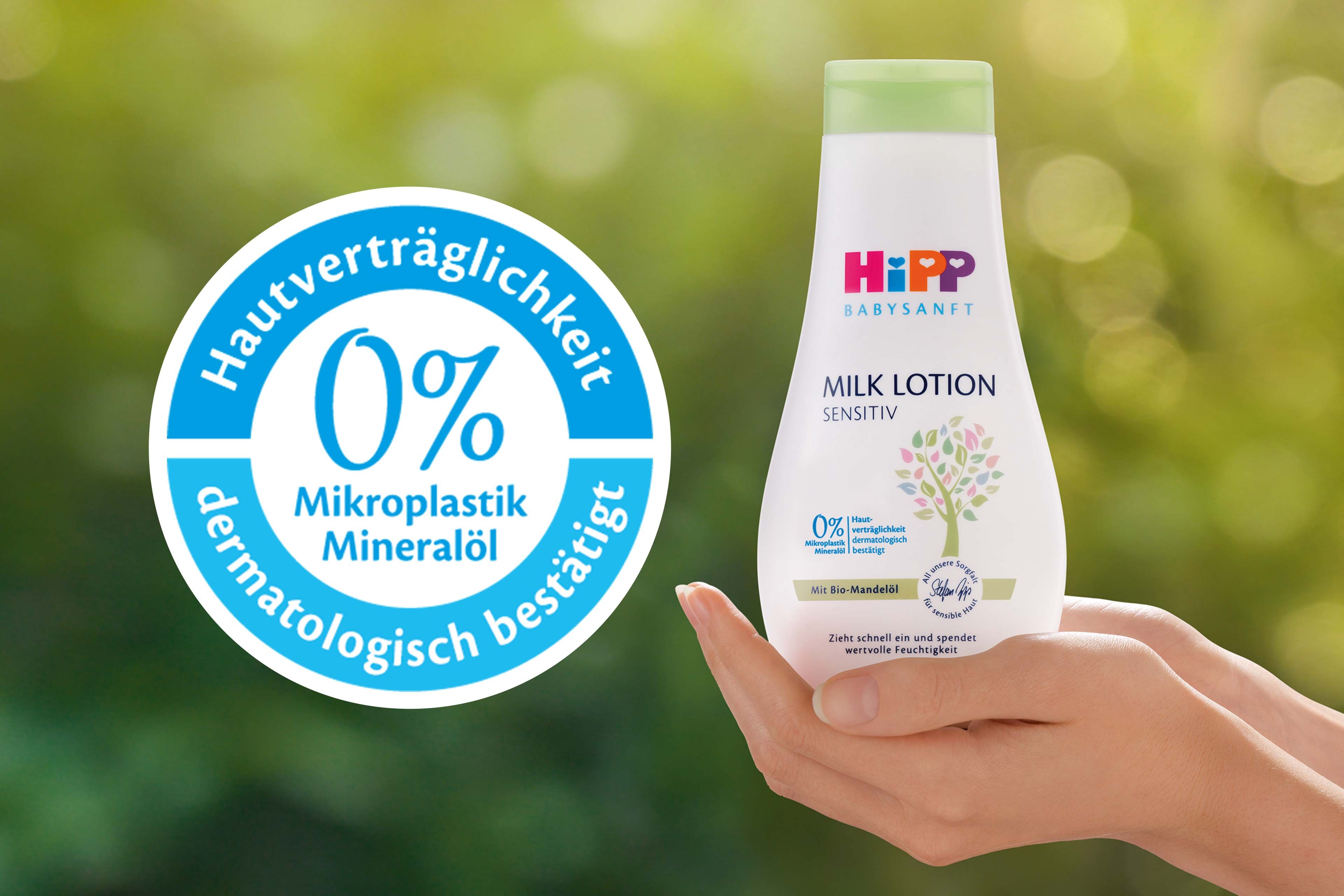 Eine Flasche eines Babypflegeprodukts mit der Aufschrift "Hipp Baby Sensitive" und einem Etikett mit der Aufschrift "0% Mikroplastik Mineralol" sowie eine Hand, die das Produkt vor einem grünen Hintergrund hält.