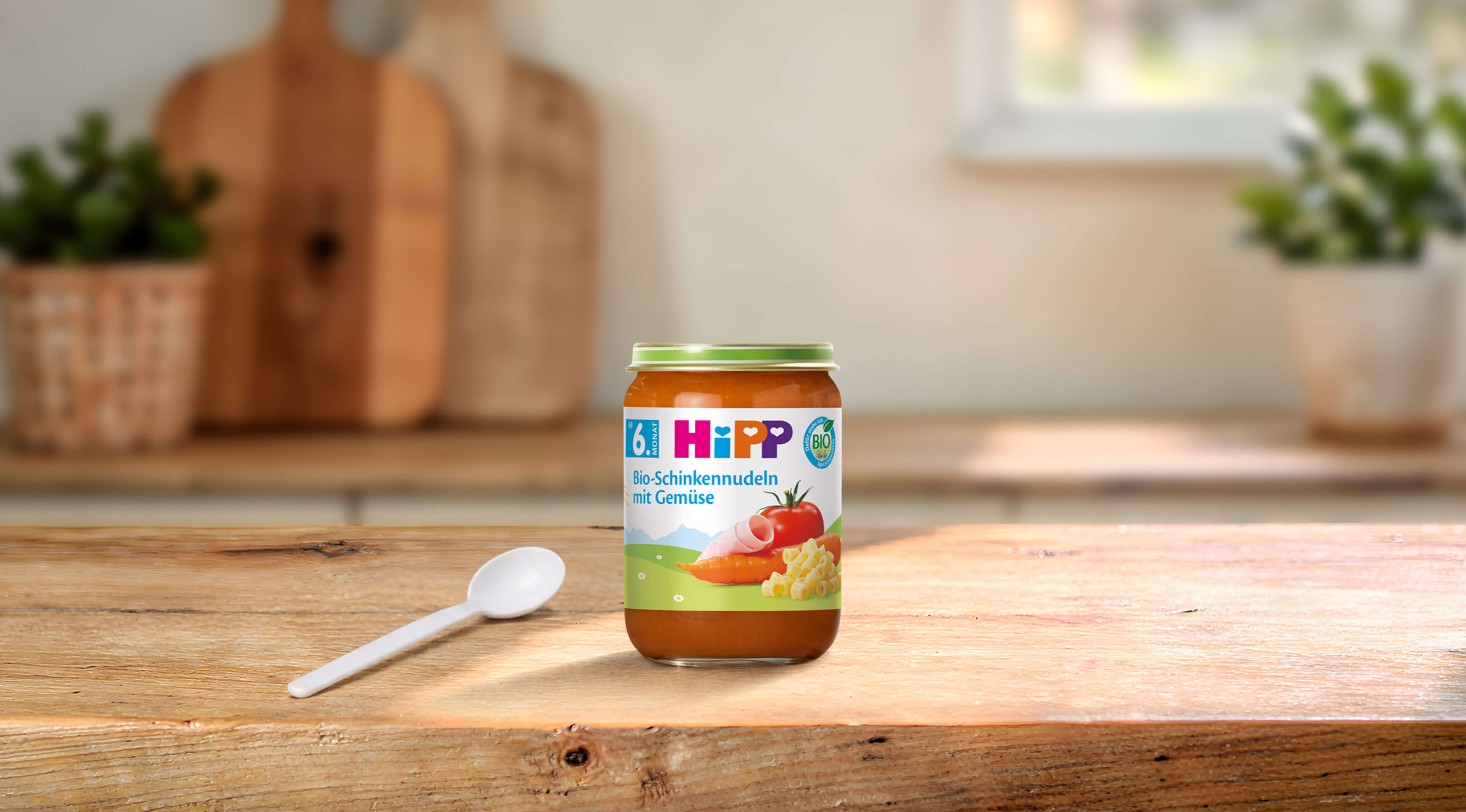 HiPP Bio-Schinkennudeln mit Gemüse 190g im Glas auf Holztisch mit Löffel in heller, gemütlicher Küchenumgebung