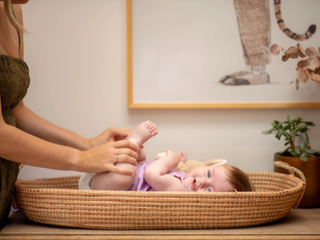 Mum changing baby in purple dress nappy, baby is smiling whilst holding her feet