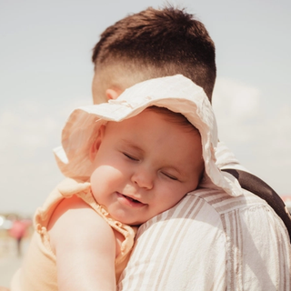 Baby in sun hat leaning on dad's shoulder